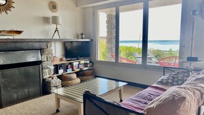 A cozy living room with a stone fireplace, a flat-screen TV, and a view of the ocean through large windows. - Villa 10 persons, first line, Lège Cap Ferret (Lège-Cap-Ferret)
