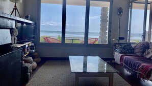 A living room with a large window overlooking the ocean, a glass coffee table, a sofa with a patterned throw, and a stone shelf with various items. - Villa 10 persons, first line, Lège Cap Ferret (Lège-Cap-Ferret)