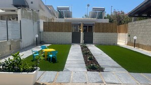 Une terrasse avec une petite table et des chaises, un étroit sentier et un parterre de fleurs.
