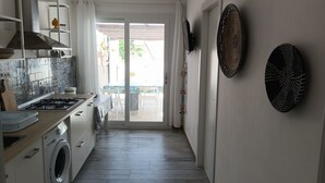 Une cuisine moderne équipée d’un lave-linge intégré, un coin repas avec une table et des chaises, et une vue sur l’extérieur à travers la porte vitrée.