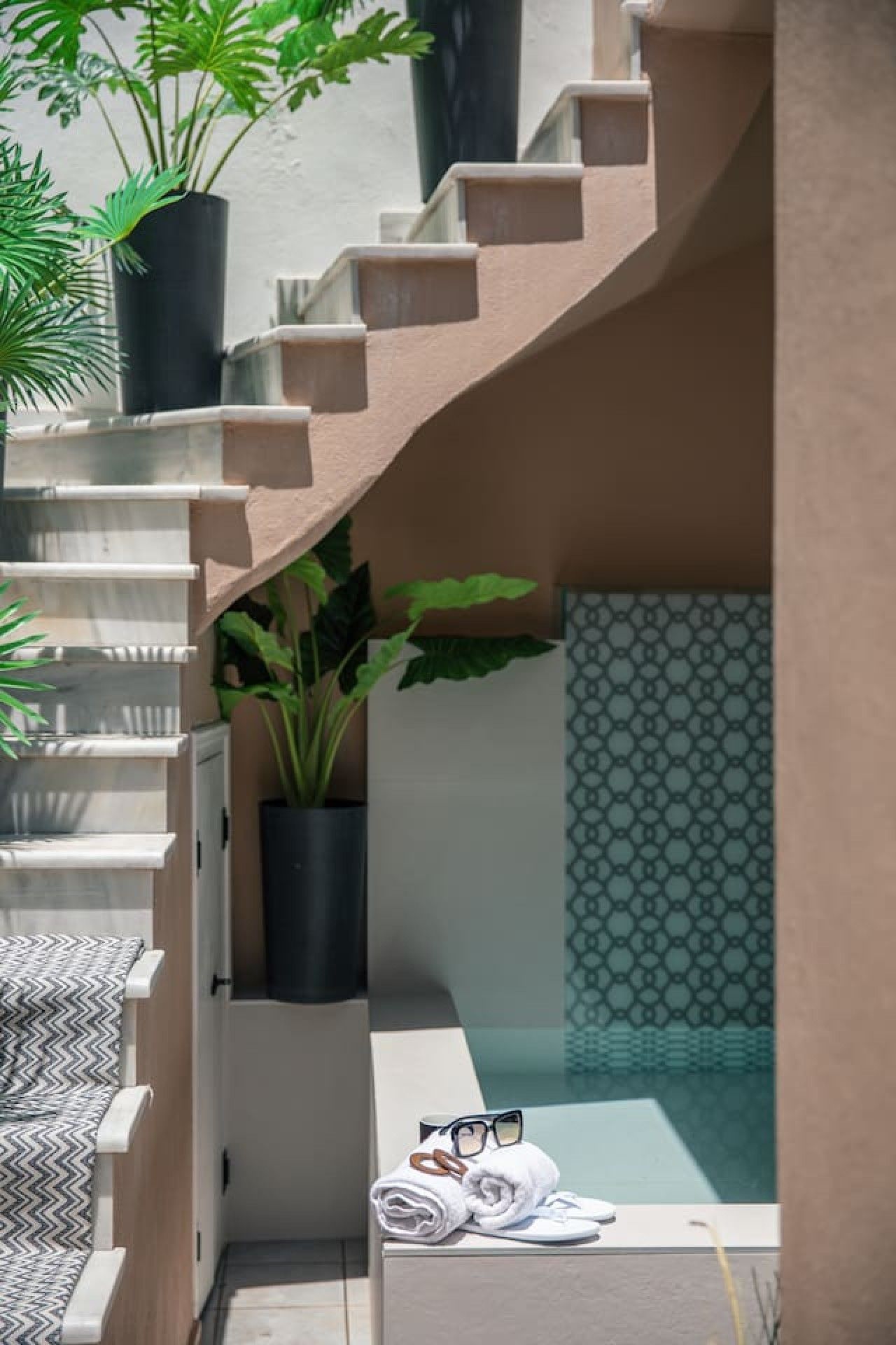 A modern staircase with a beige finish, leading to a room with a patterned wall and a small pool area.