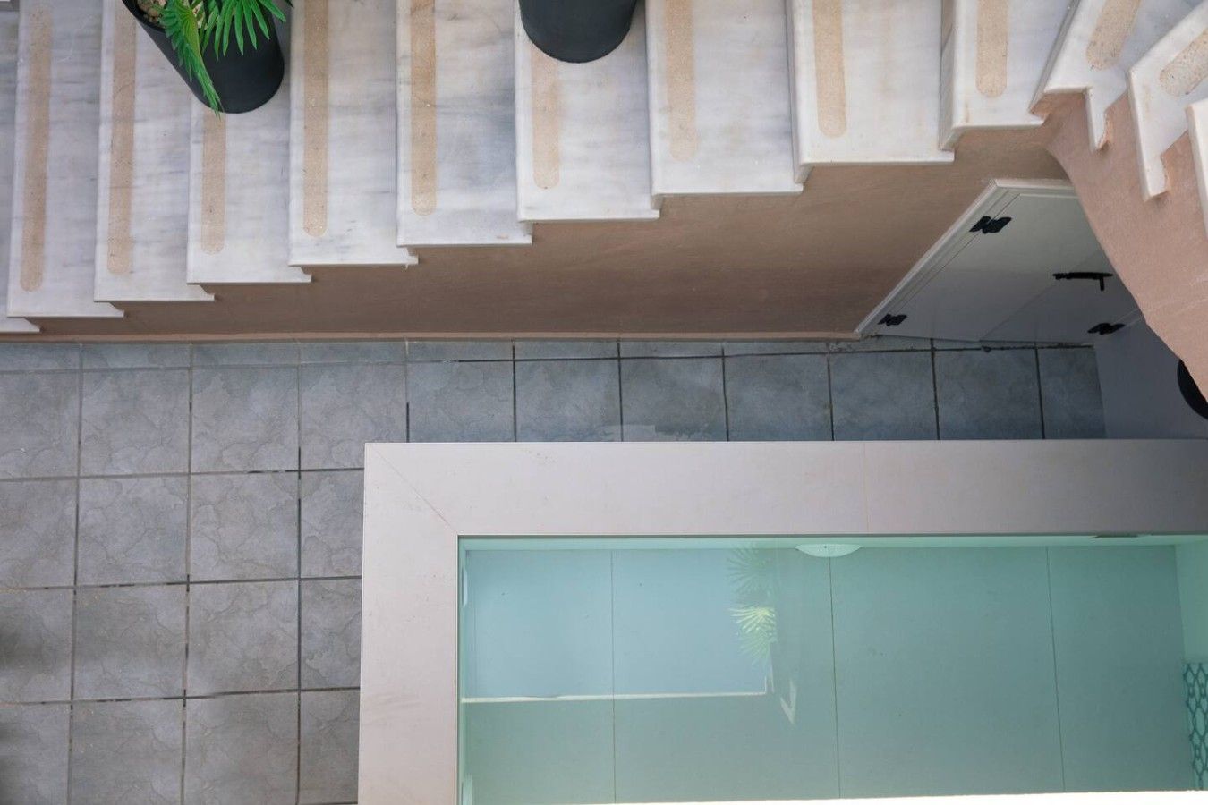 Un interior moderno con piso de baldosas, un mamparo de vidrio y una escalera frente a una pared color beige.
