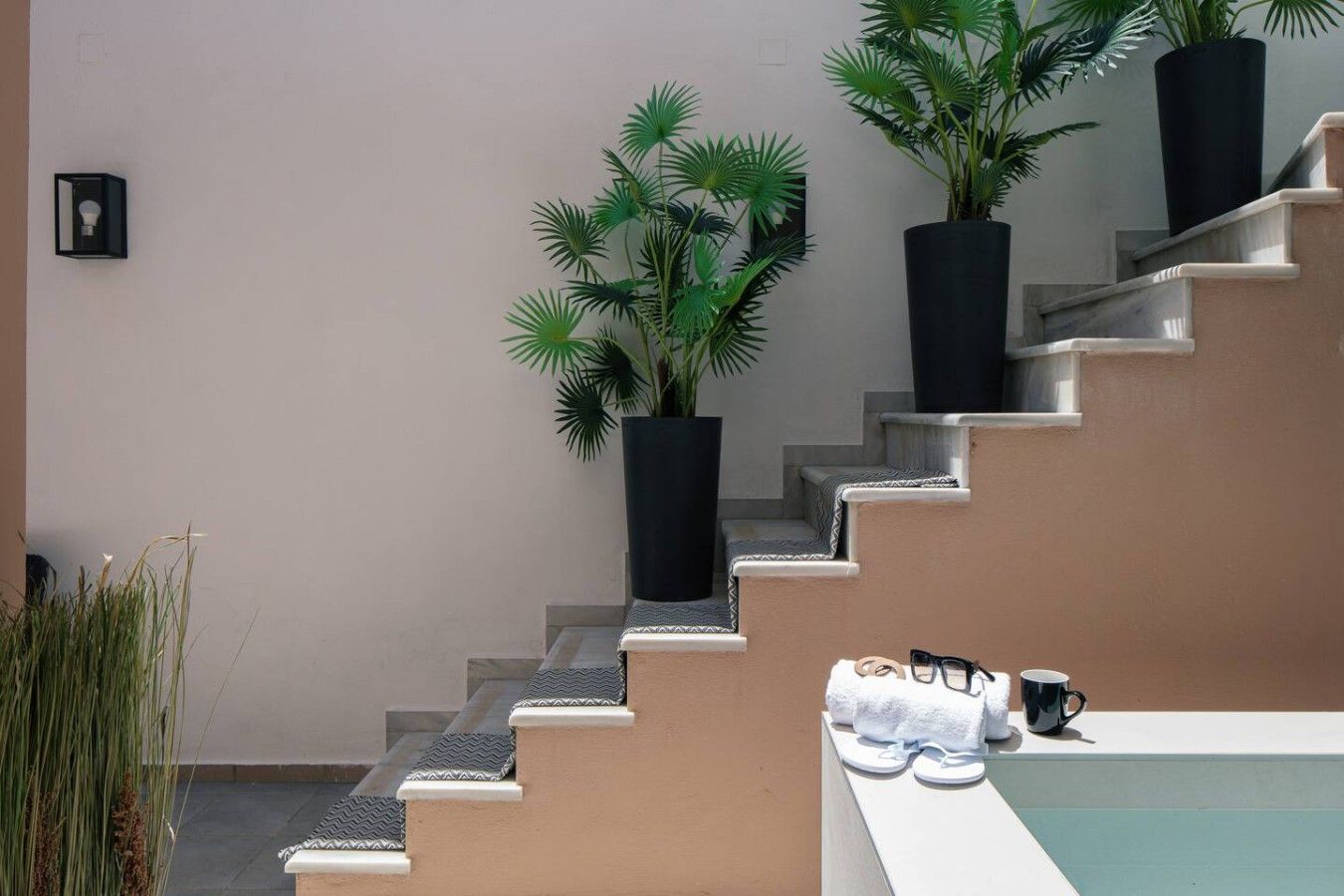 Eine Treppe mit einer beigen Wand und schwarzen Pflanzgefäßen mit Grünpflanzen.