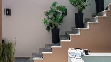 Eine Treppe mit einer beigen Wand und schwarzen Pflanzgefäßen mit Grünpflanzen.