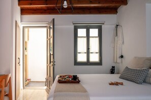 A bedroom with a bed, a window, a door, and a small table with food. - Gateway Suites - Harmony (Ρέθυμνο)