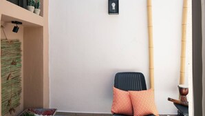 Una habitación con una silla negra, almohadas anaranjadas, una mesita con un objeto decorativo, y una lámpara fijada a la pared.