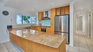 Une cuisine moderne dotée d’un plan de travail en granit, d’appareils électroménagers en acier inoxydable et de meubles en bois.