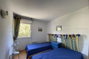 Two single beds, a wall-mounted fan, and a bedside table with a lamp make this room a comfortable retreat.