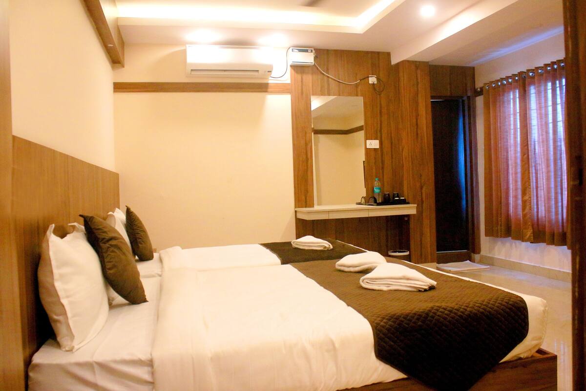 A hotel room with a bed, a mirror, a window with curtains, and a wall-mounted air conditioning unit.
