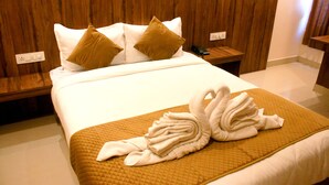 Ein Hotelzimmer mit einem hölzernen Kopfteil, einem Bett mit weißer Bettwäsche und zwei braunen Kissen, einem Nachttisch mit Telefon sowie einer Bett-Skulptur aus Handtüchern.