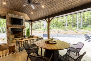 Un patio exterior con chimenea de piedra, techo de madera y una mesa redonda con sillas.
