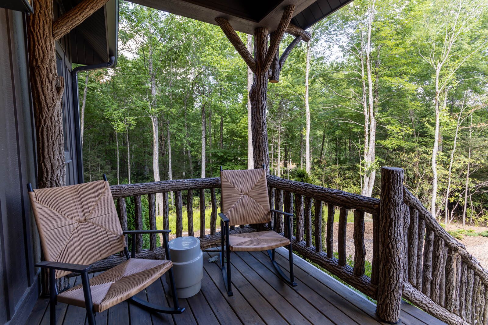 A wooden deck with two wicker chairs and a small table, overlooking a forested area.