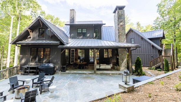 Una casa grande y moderna con chimenea de piedra, mobiliario exterior y un patio cubierto.