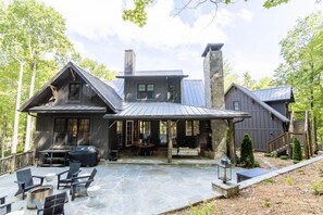 Une grande maison moderne dotée d’une cheminée en pierre, d’un espace salon extérieur et d’un patio couvert.