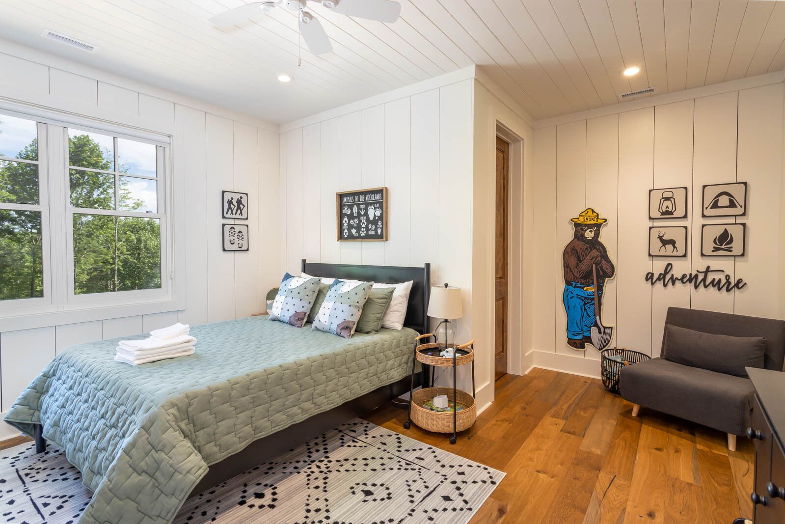 A bedroom with a bed, a chair, a lamp, and a wall with framed pictures and a bear illustration.