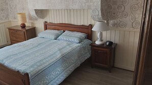 A bedroom with a wooden bed, two bedside tables with lamps, a radiator, and patterned wallpaper.