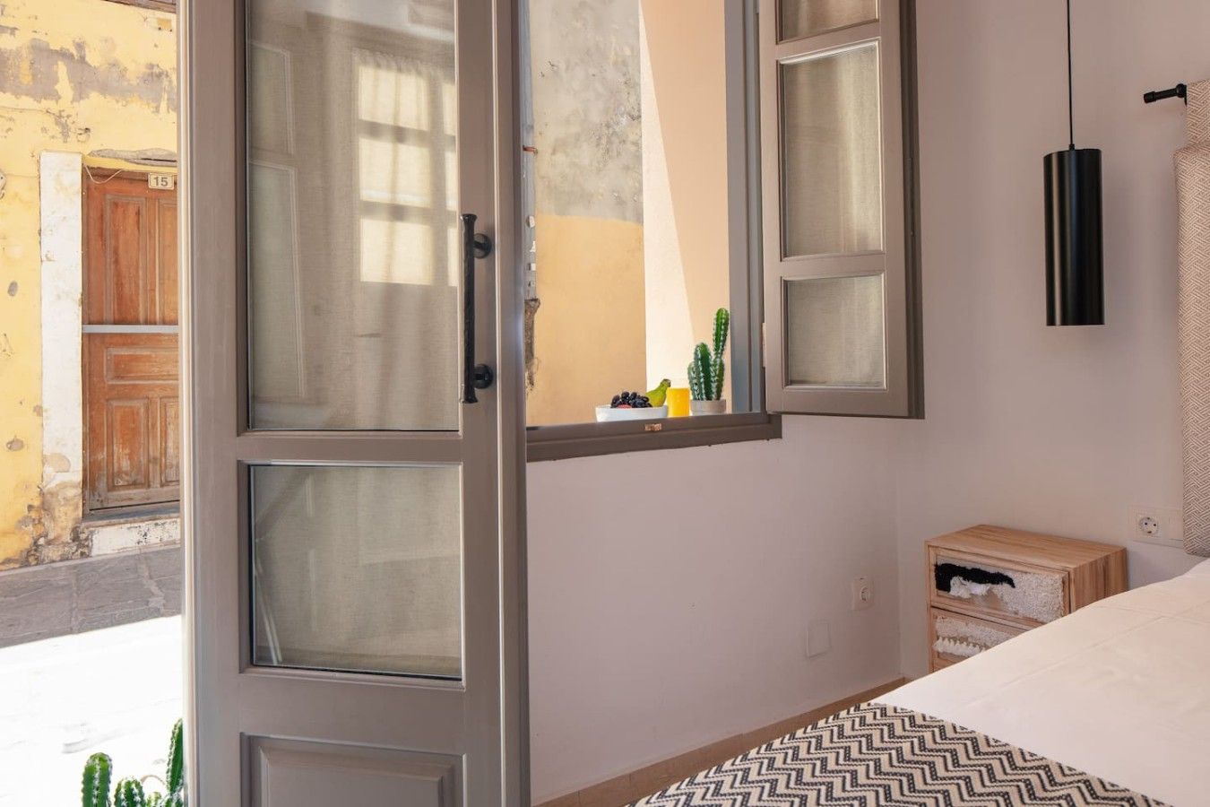 Un dormitorio con una cama, una ventana con cortinas, una mesita de noche y una lámpara de pared.