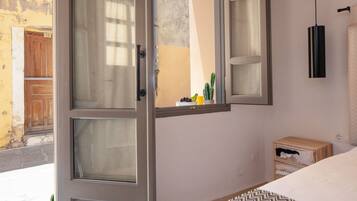 Un dormitorio con una cama, una ventana con cortinas, una mesita de noche y una lámpara de pared.