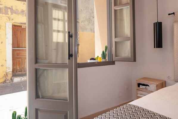 Un dormitorio con una cama, una ventana con cortinas, una mesita de noche y una lámpara de pared.