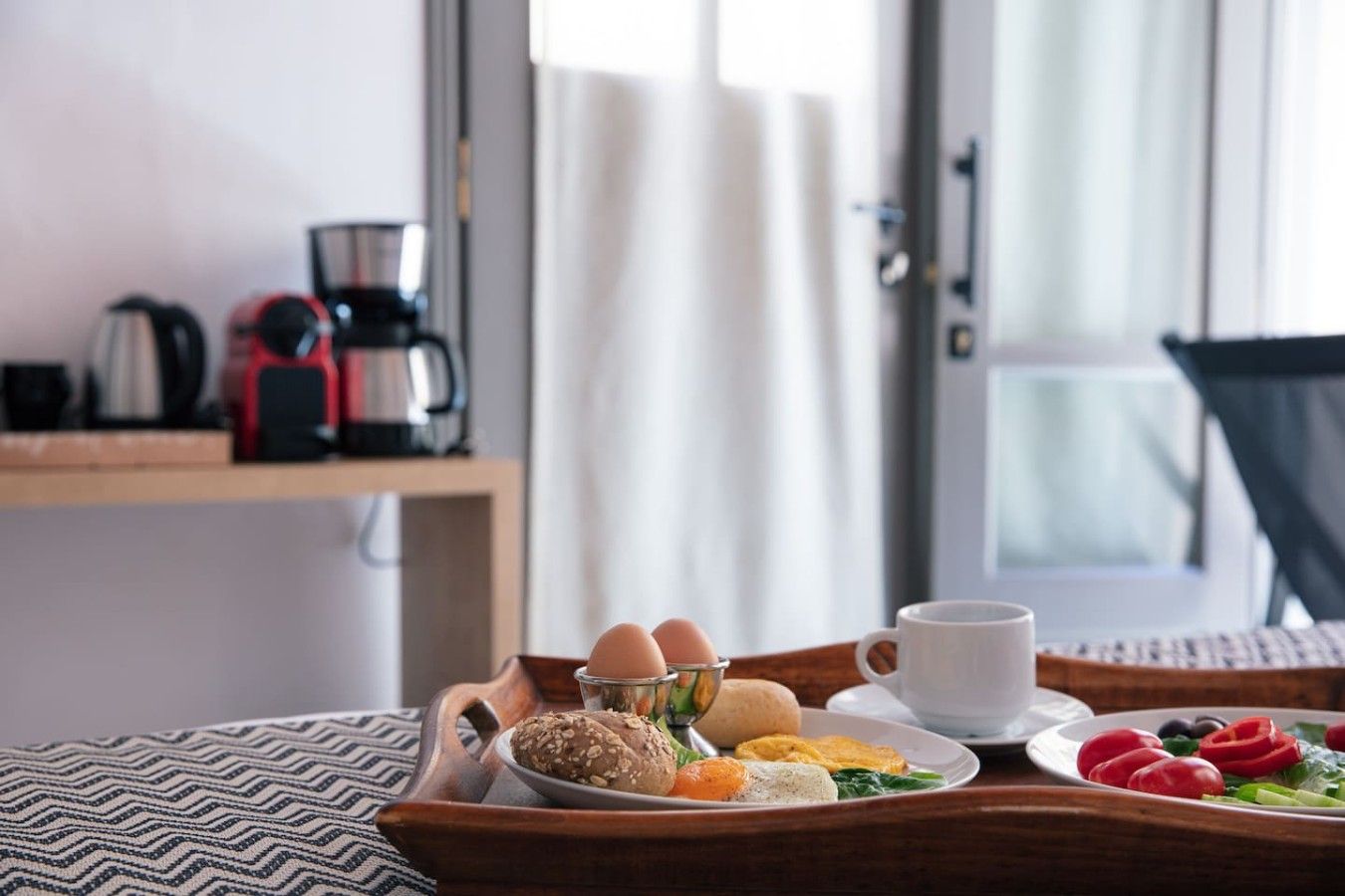 Bandeja de desayuno con huevos, pan y frutas sobre una mesa de madera en una habitación de hotel.