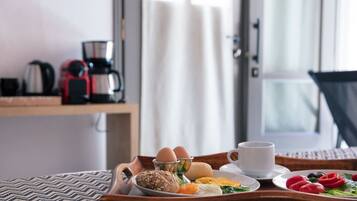 Bandeja de desayuno con huevos, pan y frutas sobre una mesa de madera en una habitación de hotel.