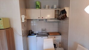 A compact kitchen with a sink, stove, and a washing machine. There's a yellow table with a decorative bowl. - Beachside Retreat: Cozy 1BR Apt with Balcony, WiFi & Parking (Seignosse)