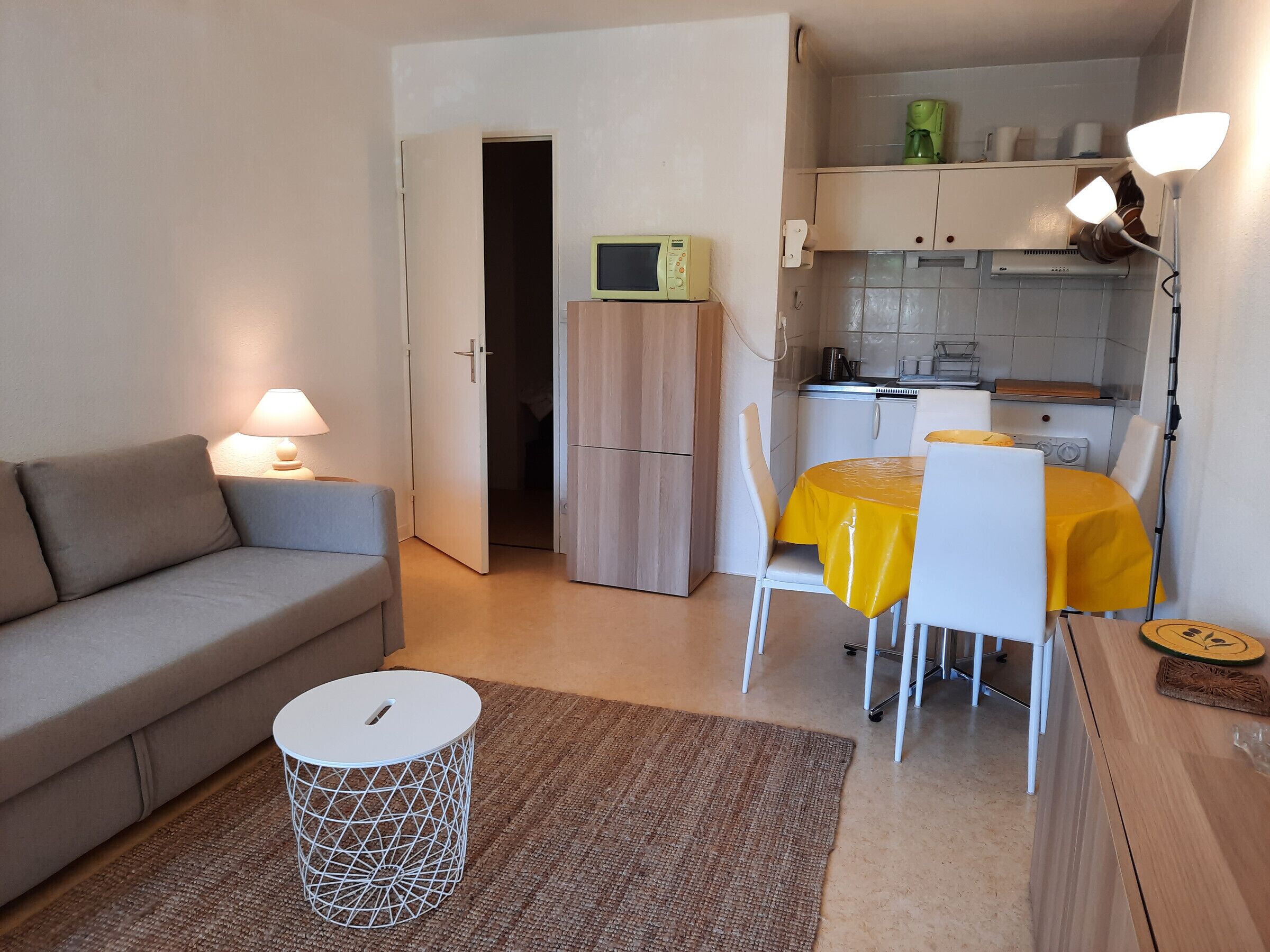 Un espacio habitable compacto con sofá, una mesa de comedor con sillas, una pequeña cocina y un microondas.