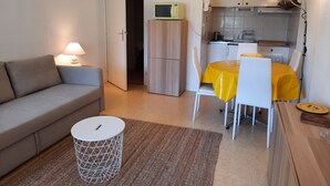 A compact living space with a sofa, a dining table with chairs, a small kitchen area, and a microwave. - Beachside Retreat: Cozy 1BR Apt with Balcony, WiFi & Parking (Seignosse)