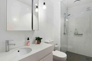 Features a sleek vanity, large mirror, and modern light fixtures, along with a glass-enclosed shower area with handheld showerhead and faucet.