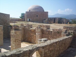 Ancient ruins with a dome structure, stone walls, and a mountainous backdrop.