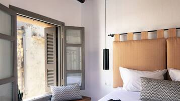 A bedroom with a bed, pillows, a bedside table, and a window with shutters.