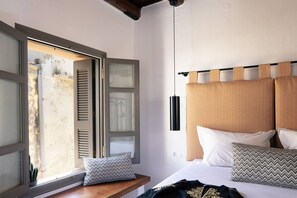 A bedroom with a bed, pillows, a bedside table, and a window with shutters. - Gateway Suites - Elpida (Ρέθυμνο)