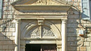 A stone building with a large wooden door, a decorative arch, and a small plaque.