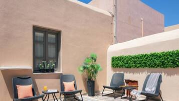 An outdoor seating area with wicker chairs and cushions, a window with potted plants, and a wall-mounted green plant.