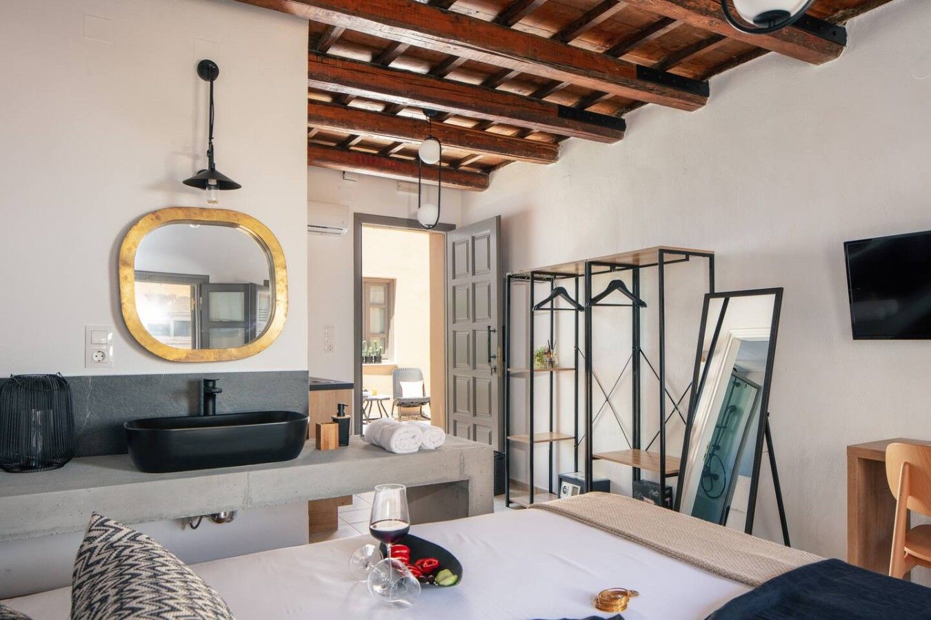 A hotel room with a large bed, a round mirror, a black sink, and a TV mounted on the wall.