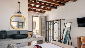 Ein Hotelzimmer mit einem großen Bett, einem runden Spiegel, einem schwarzen Waschbecken und einem an der Wand befestigten Fernseher.