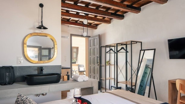 A hotel room with a large bed, a round mirror, a black sink, and a TV mounted on the wall.