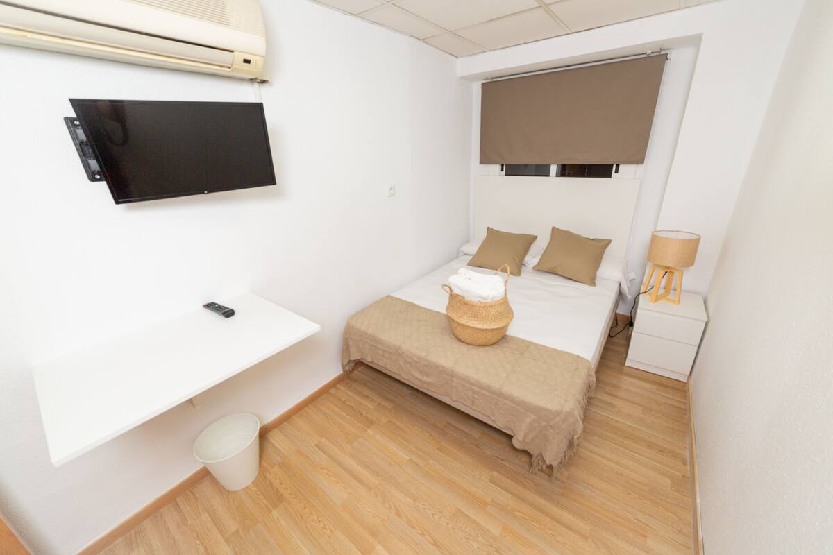 A compact bedroom with a bed, bedside table, lamp, and a mounted TV.