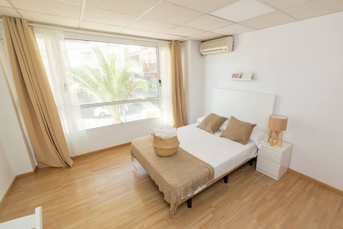 A bedroom with a bed, bedside table, lamp, and a window with curtains.