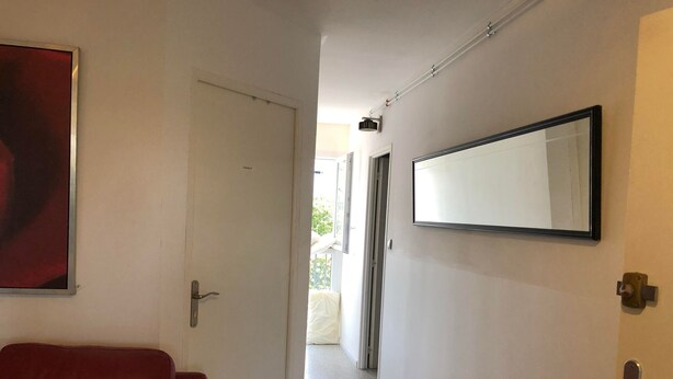 Un couloir avec une porte blanche, un canapé en cuir rouge, un grand miroir et un luminaire fixé au plafond.