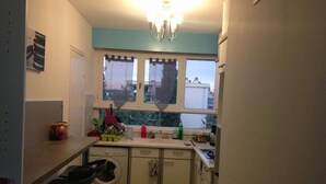 Une cuisine compacte équipée d’un lave-linge, d’un évier et d’une fenêtre donnant sur un quartier résidentiel.