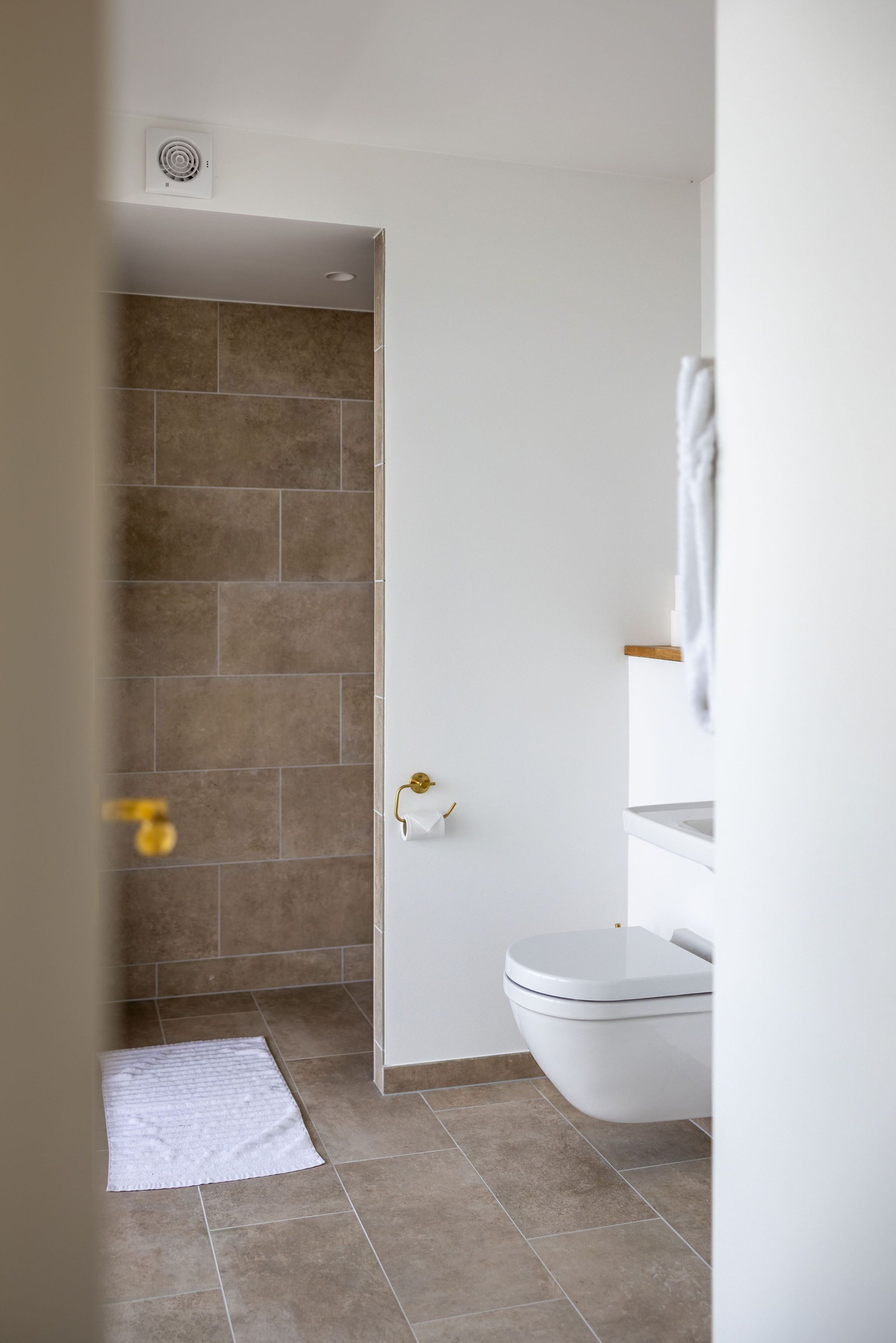 A bathroom with a white toilet, a white sink, and a shower area with brown tiles.