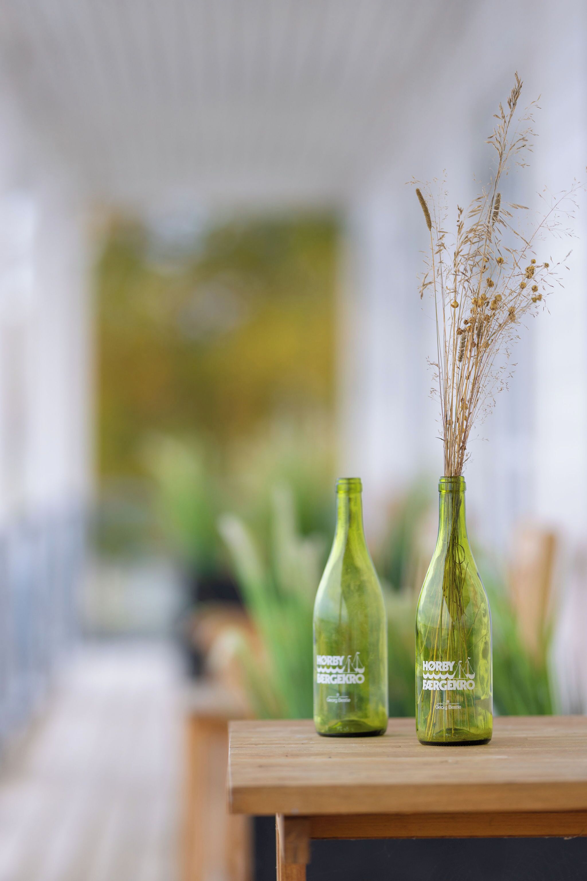 Dos botellas de vidrio con plantas secas sobre una mesa de madera.
