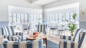 A spacious hotel lobby with striped armchairs, a round wooden table with drinks, and large windows offering views of the city. - Hørby Færgekro (Holbaek)