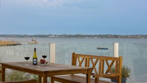 A wooden table with a bottle of wine and glasses, overlooking a calm body of water with a distant shoreline and a small boat. - Hørby Færgekro (Holbaek)