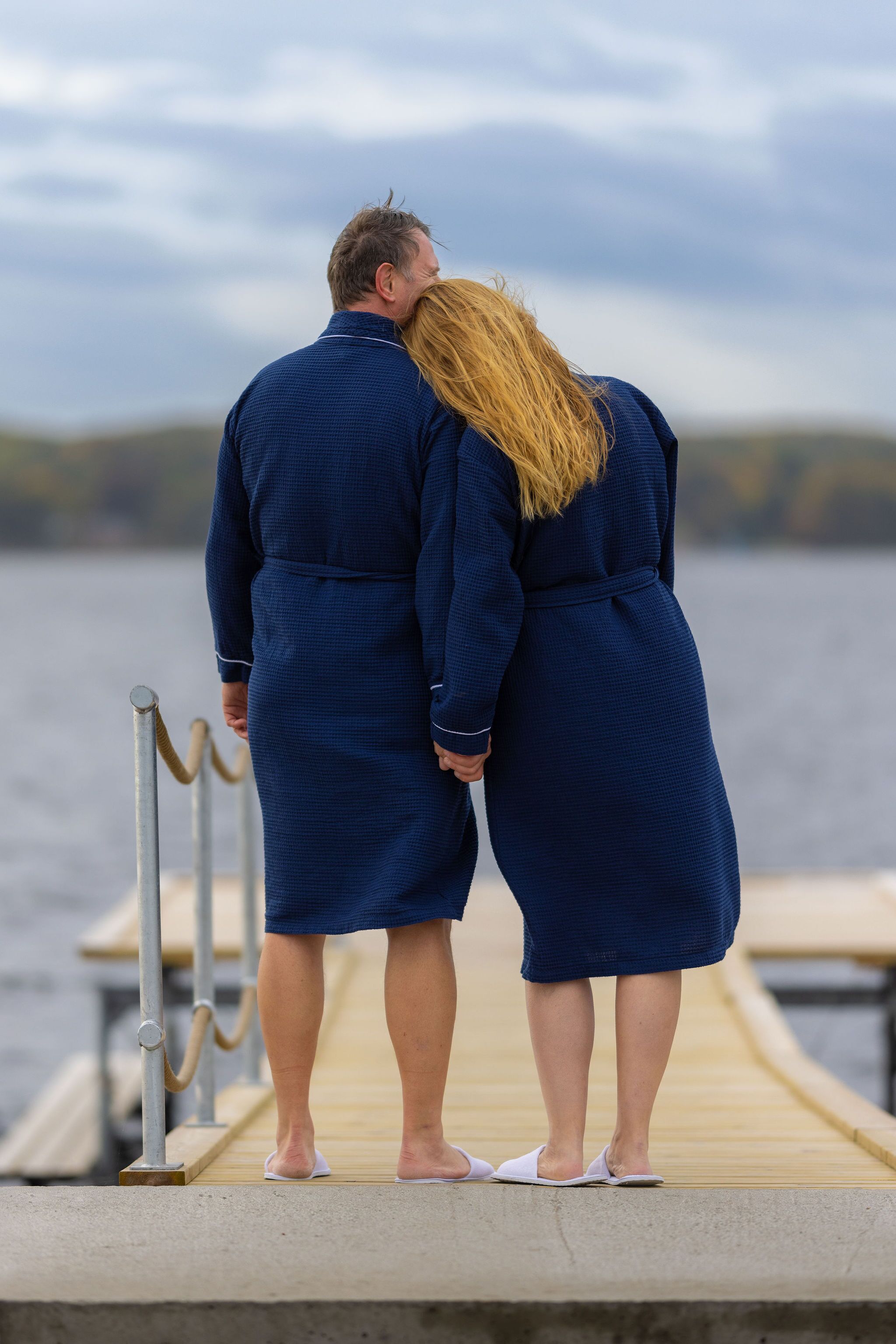 Una pareja de pie sobre un muelle de madera junto al agua.