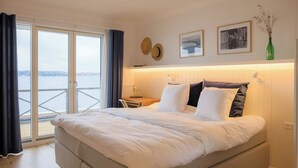 A hotel room with a bed, a desk, a chair, a view through a glass door, and wall decorations. - Hørby Færgekro (Holbaek)