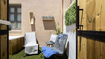 A small outdoor seating area with two lounge chairs, a wooden door, and a wall-mounted planter with greenery.