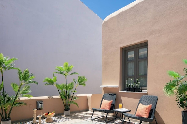 A sunlit outdoor seating area with two wicker chairs, a small table, and potted plants.