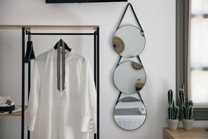 A white blouse hanging on a black hanger, a wall-mounted mirror with three circular mirrors, and two potted cacti on a wooden table. - Gateway Suites - Pathos (Ρέθυμνο)